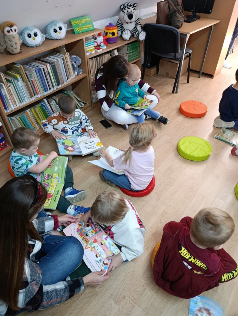 Dzieci słuchają opowieści wśród bibliotecznych regałów